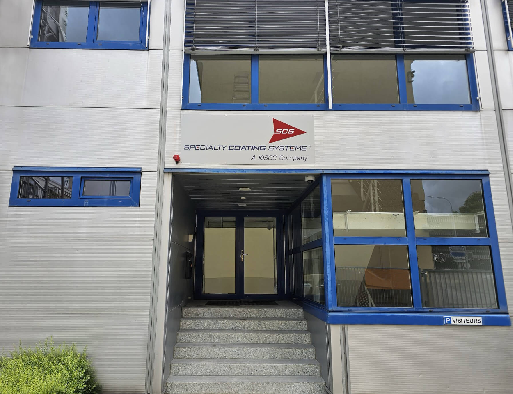 Entrance of Switzerland coating facility with a sign reading "Specialty Coating Systems" above the door and blue-framed windows.